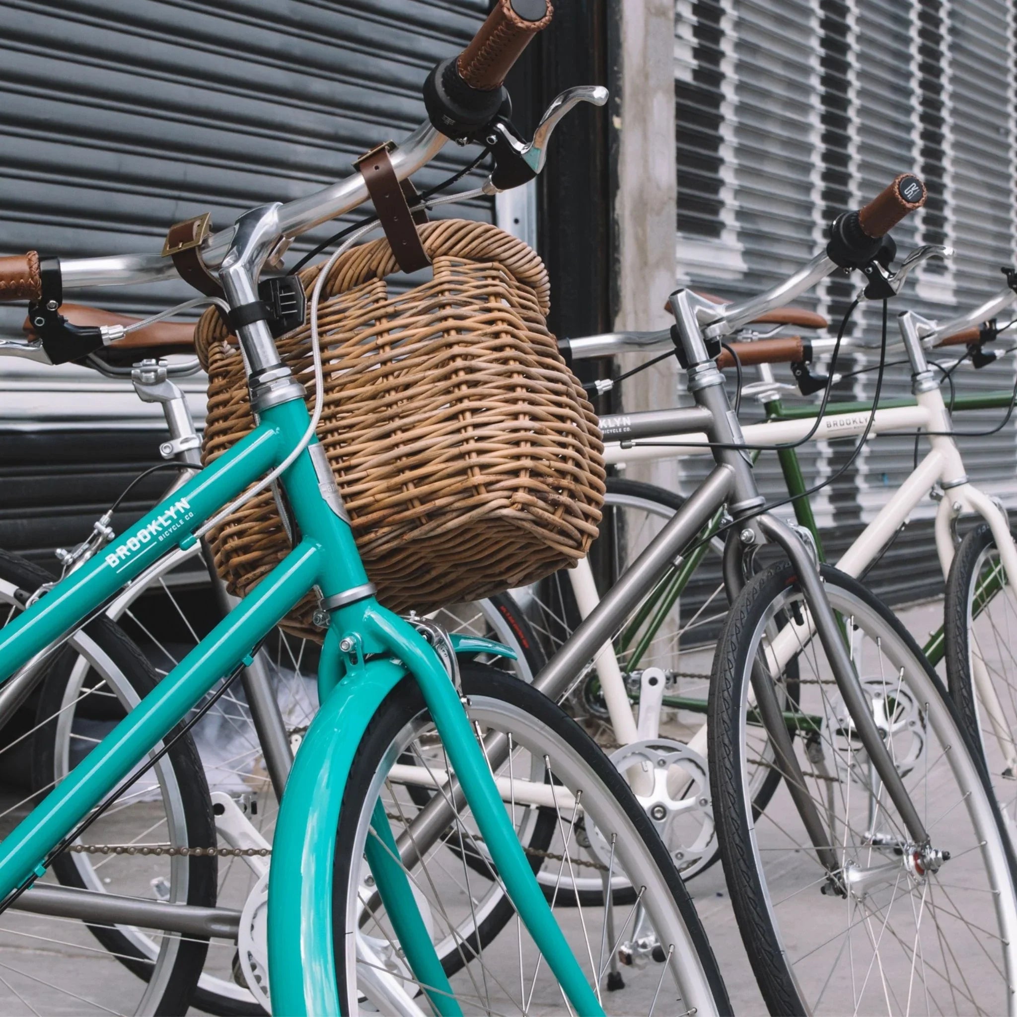 Sea Glass Franklin with a rattan basket hanging from its handlebars, with 3 bikes behind it