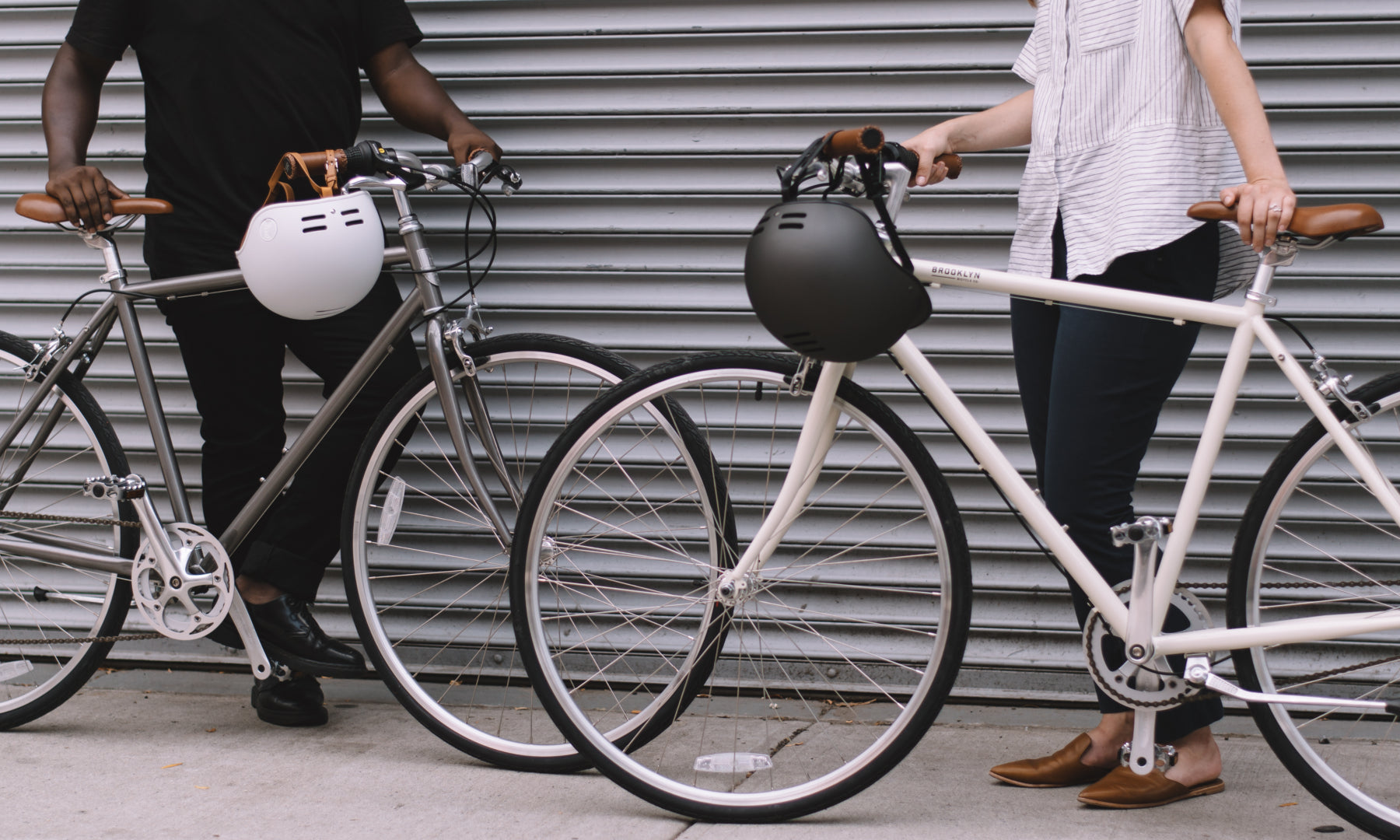 Two people standing with bicycles, helmets hanging from handlebars